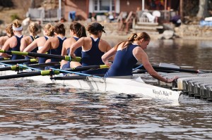 Members of the Women’s Rowing Team push off from the dock at the boathouse on Coventry Lake in their new racing shell, named in honor of retired psychology professor Sam Witryol. Photo by Peter Morenus   