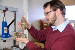 <p>Andrew Bush, assistant professor of ecology and evolutionary biology, looks at pieces of New York sandstone with brachiopod fossils embedded in them. Photo by Jessica Tommaselli</p>