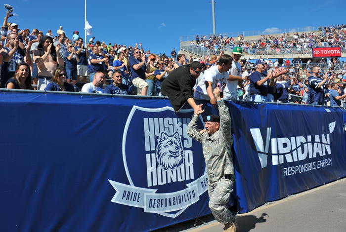 <p>Major Glen Colby, recuiting and operations officer for UConn ROTC  offers high fives to fans at Rentscher Stadium as current and former military were recognized on the field. Morrell served in the US Navy. Photo by Peter Morenus.</p>