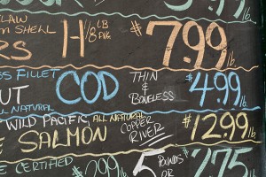 A chalk board lists the prices of fish.
