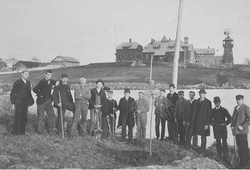 As a departing gift to the college, members of the Class of 1893, the first to graduate after Storrs Agricultural College was designated as Connecticut's land grant institution, plant a willow tree in front of Duck Pond (now Swan Lake). The pole behind them held the line to the only telephone on campus, located in the President's Office in Whitney Hall (seen on left). (University Photograph Collection, Archives &amp; Special Collections)