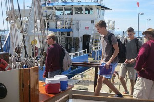 Undergraduates from left, Dana Lewis, Peter Wojtowicz, and Andrew Perkins board the Mystic Whaler before class, with a crew member looking on. (Nathaniel Trumbull/UConn Photo)