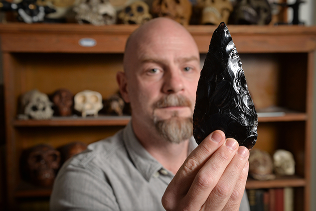 Daniel Adler, associate professor of anthropology, with a stone tool at his office in Beach Hall. (Peter Morenus/UConn Photo)