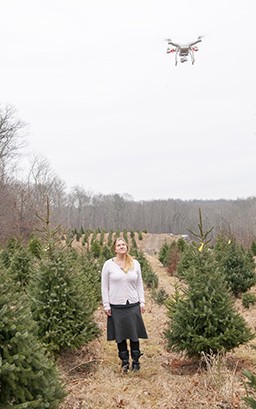 Jill WEgrzyn looks up at a drone flying overhead at a Christmas tree farm. Researchers now use drone technology to survey forests and orchards. (Sean Flynn/UConn Photo)
