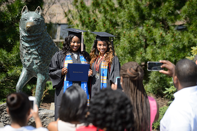 Khortney Hundley of Hamden, left, and Begum Abadin of New Britain pose for a photo with the statue of Jonathan the husky outside Gampel Pavilion following their Commencement ceremonies on May 10, 2015. (Peter Morenus/UConn Photo)