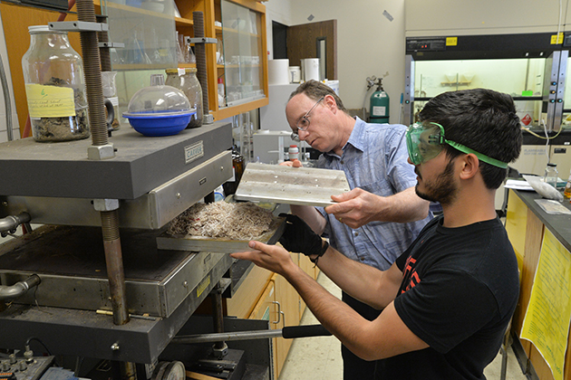 Daniel Kloyzner ‘16 (ENG), right, with Richard Parnas, a professor of chemical, materials, and biomolecular engineering, place a loaded mold into the press in preparation for compression-molding a particleboard composites sample made from a combination of waste carpet, biomass fibers, inorganic additives, and thermoset resin. (Sean Flynn/UConn Photo)