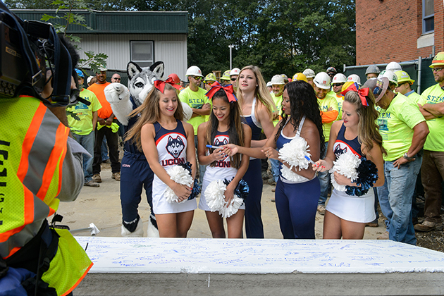 Cheerleaders and Jonathan the Husky sign a concrete panel to be hoisted to the roof during the topping off ceremony for the STEM residence hall on Sept. 14, 2015. (Peter Morenus/UConn Photo)