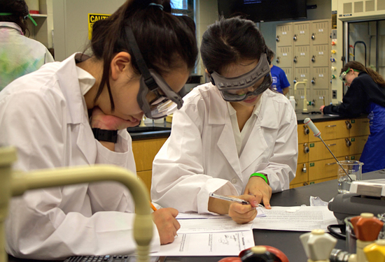 Students in white coats filling out lab sheets
