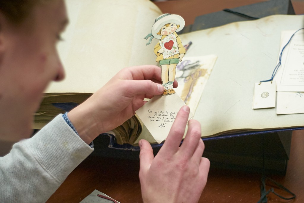 Charles Smart '18 (CLAS) reviews a scrapbook from the early 1920s kept by Flora Howe '25 at the University Archives on April 6, 2016. (Peter Morenus/UConn Photo)