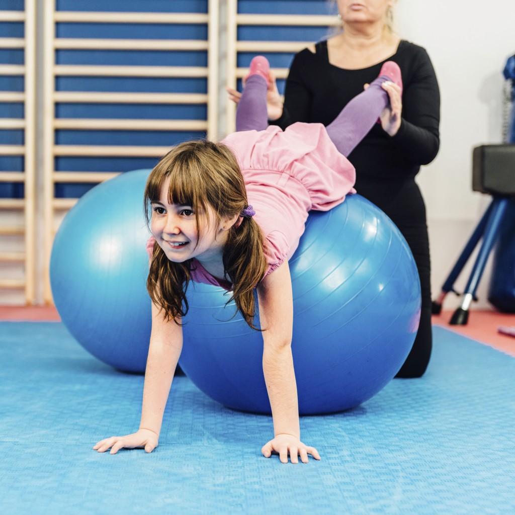 Girl exercising on pilates ball with instructor's help. (iStock Photo)