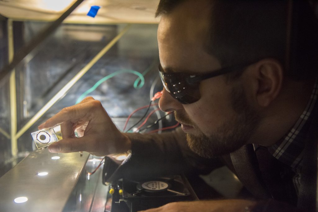 University of Connecticut researcher Justin Luria observes a sample of a cadmium telluride solar cell that is being tested under artificial sunlight in UConn’s NanoMeasurements lab. (Photo by Ryan Glista/UConn)
