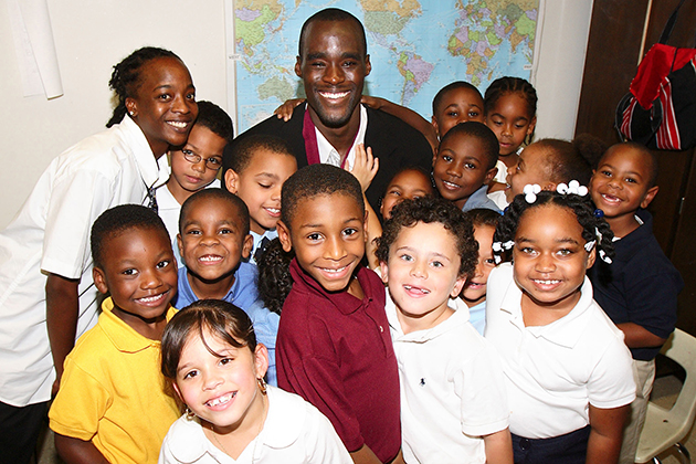 Former men's basketball player Emeka Okafor, with children at the Clark Elementary School in Hartford, after announcing his $250,000 gift to the Husky Sport program. In the back row, at left, is Lashika James, a paraprofessional at the school. Husky Sport, developed by kinesiology professor Jennifer Bruening, uses UConn students as mentors in nutrition and life skills, and encourages children to take part in sports and physical activities.