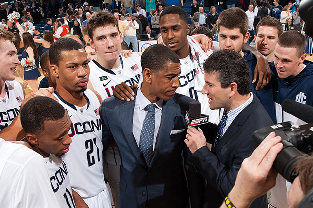 Members of the men's basketball team rally around head coach Kevin Ollie as he speaks with ESPN's Andy Katz during the game against Syracuse on Feb. 13, 2013. The Huskies beat Syracuse. (Steven Slade '89 (SFA) for UConn)