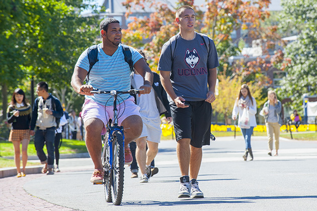 Groups of students walk across campus, including a student on a bike. (Sean Flynn/UConn Photo)