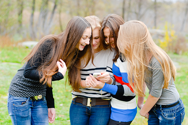 A group of teenagers crowd around to look at a smartphone one of them is holding. (Shutterstock/UConn Health Photo)