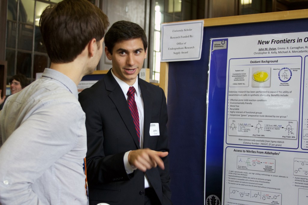 John Ovian ’17 (CLAS) explains his research in chemistry to a fellow student at the 19th annual Frontiers in Undergraduate Research Poster Exhibition. (UConn Photo/Sydney Lauro ’17 (CLAS))