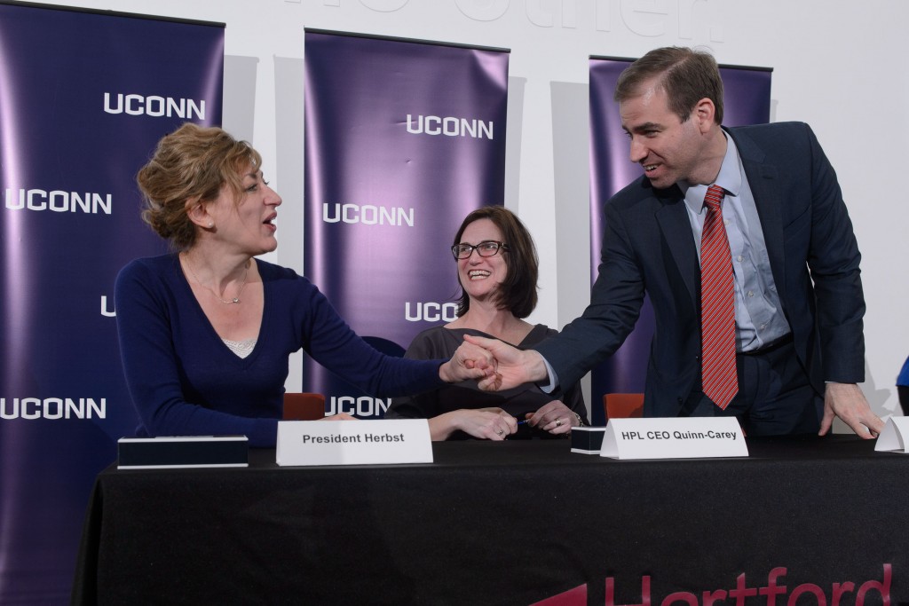 President Susan Herbst, left, HPL CEO Bridget Quinn-Carey and Mayor Luke Bronin shake hands on April 21, 2016 after signing an agreement to host the new downtown UConn Hartford library at the Hartford Public Library. (Peter Morenus/UConn Photo)
