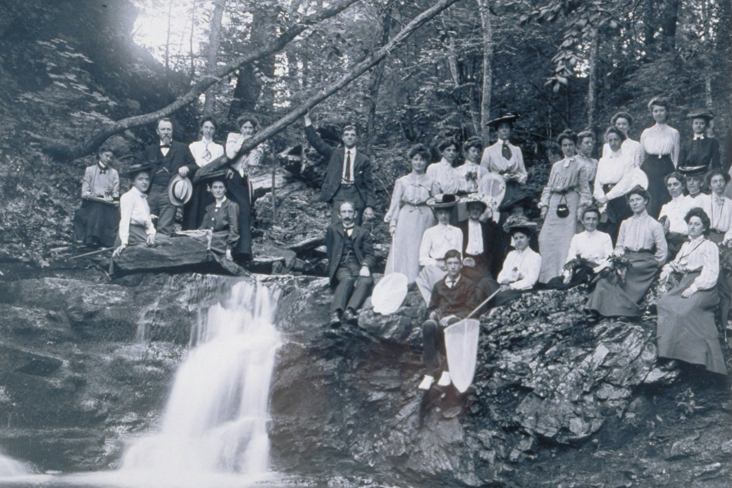 The Connecticut Agricultural College Summer School Picnic, 1907: Twenty-five women and four men sitting on rocks around a small waterfall in the woods off Codfish Falls Road in Mansfield. (University Photograph Collection, Archives & Special Collections, UConn Libraries)