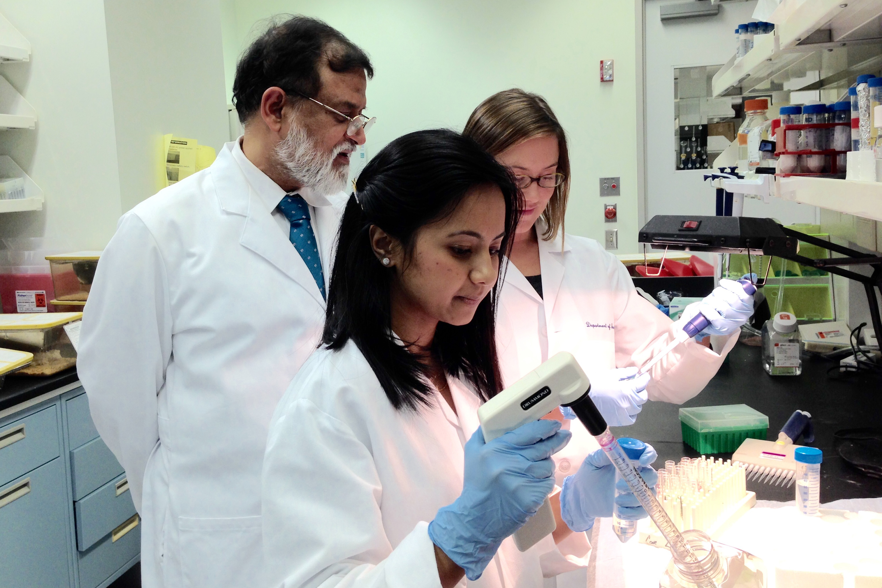 Pramod Srivastava (left), director of the Carole and Ray Neag Comprehensive Cancer Center at UConn Health, oversees students Nandini Acharya (foreground) and Stephanie Floyd in his lab. (Carolyn Pennington/UConn Health Photo)
