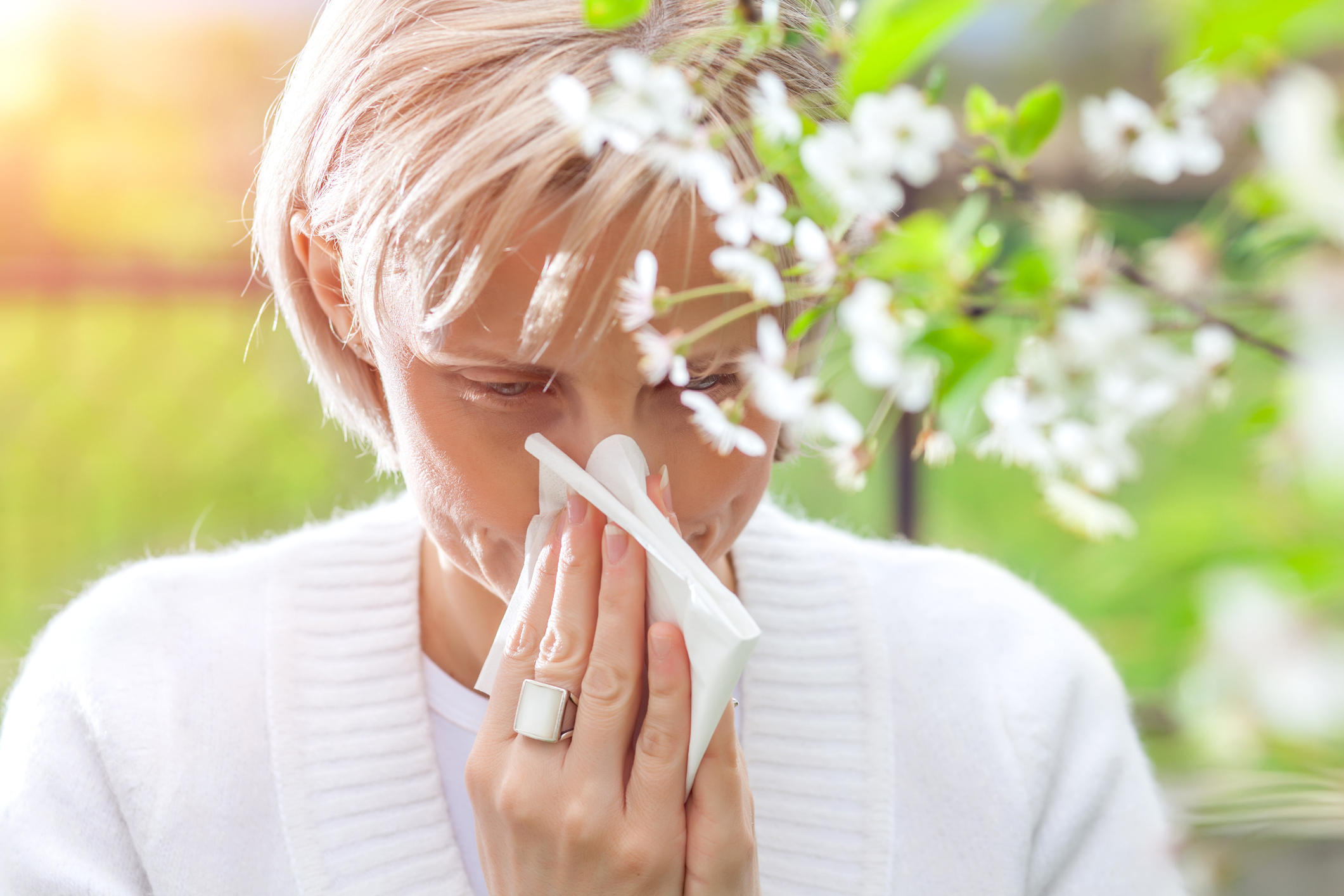 Woman sneezing, standing next to a tree in bloom. (Getty Images)