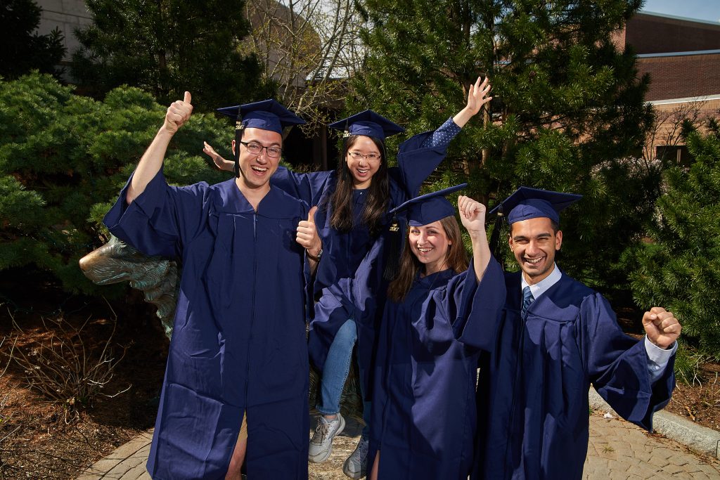From left, Christopher Chapman '17 (CLAS), Isabel Nip '17 (CLAS), Danielle Deschene '17 (CLAS), and Shaharyar Zuberi '17 (CLAS) wear the new blue commencement caps and gowns while posing next to the Husky statue. (Peter Morenus/UConn Photo)