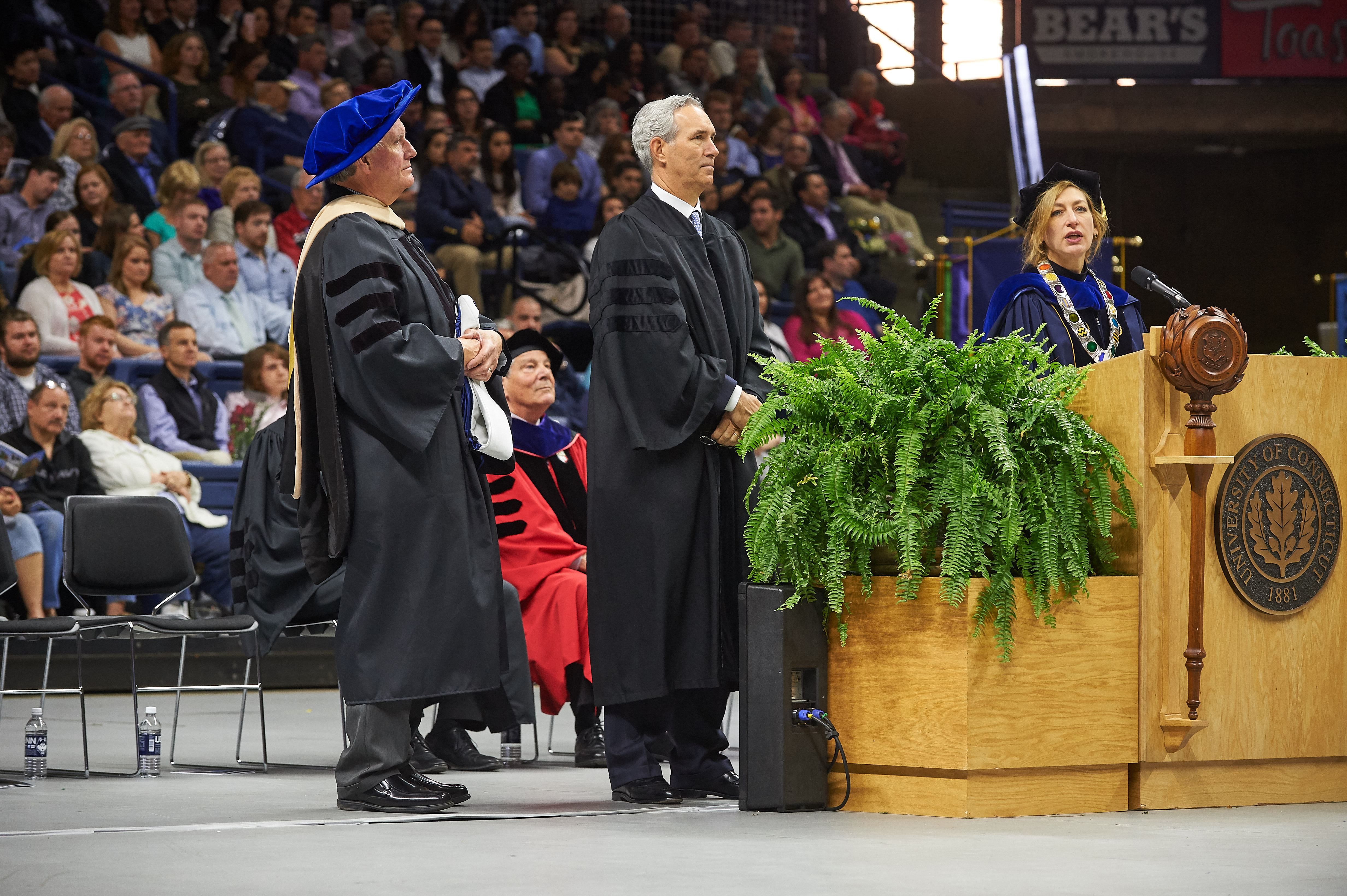 Douglas Elliot '82 (BUS), center, listens as President Susan Herbst, right, reads the citation and Lawrence Gramling, associate dean, holds a hood as Elliot receives an honorary degree during the School of Business Commencement ceremony at Gampel Pavilion on May 7, 2017. (Peter Morenus/UConn Photo)