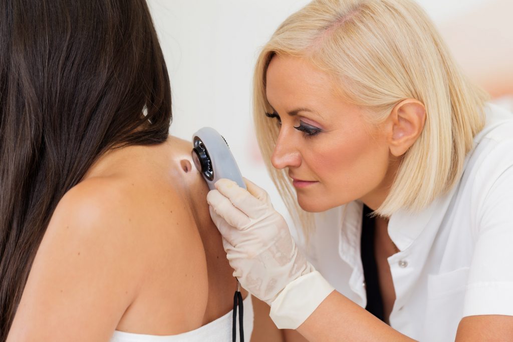 Female dermatologist examining female patient's skin with dermascope, carefully looking for signs of skin cancer. (Getty Images)