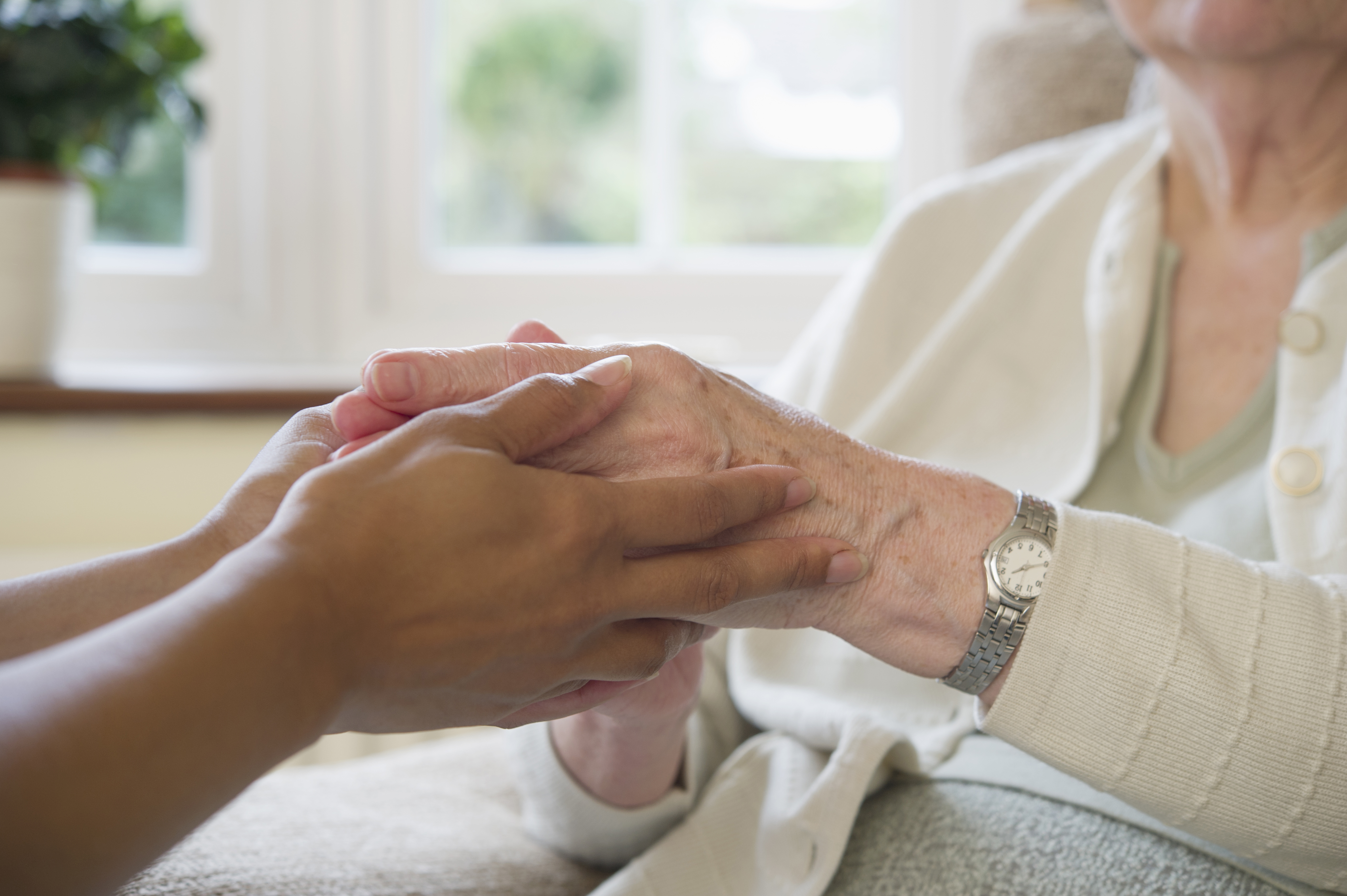 Close up of older woman and home caretaker holding hands. (Getty Images)