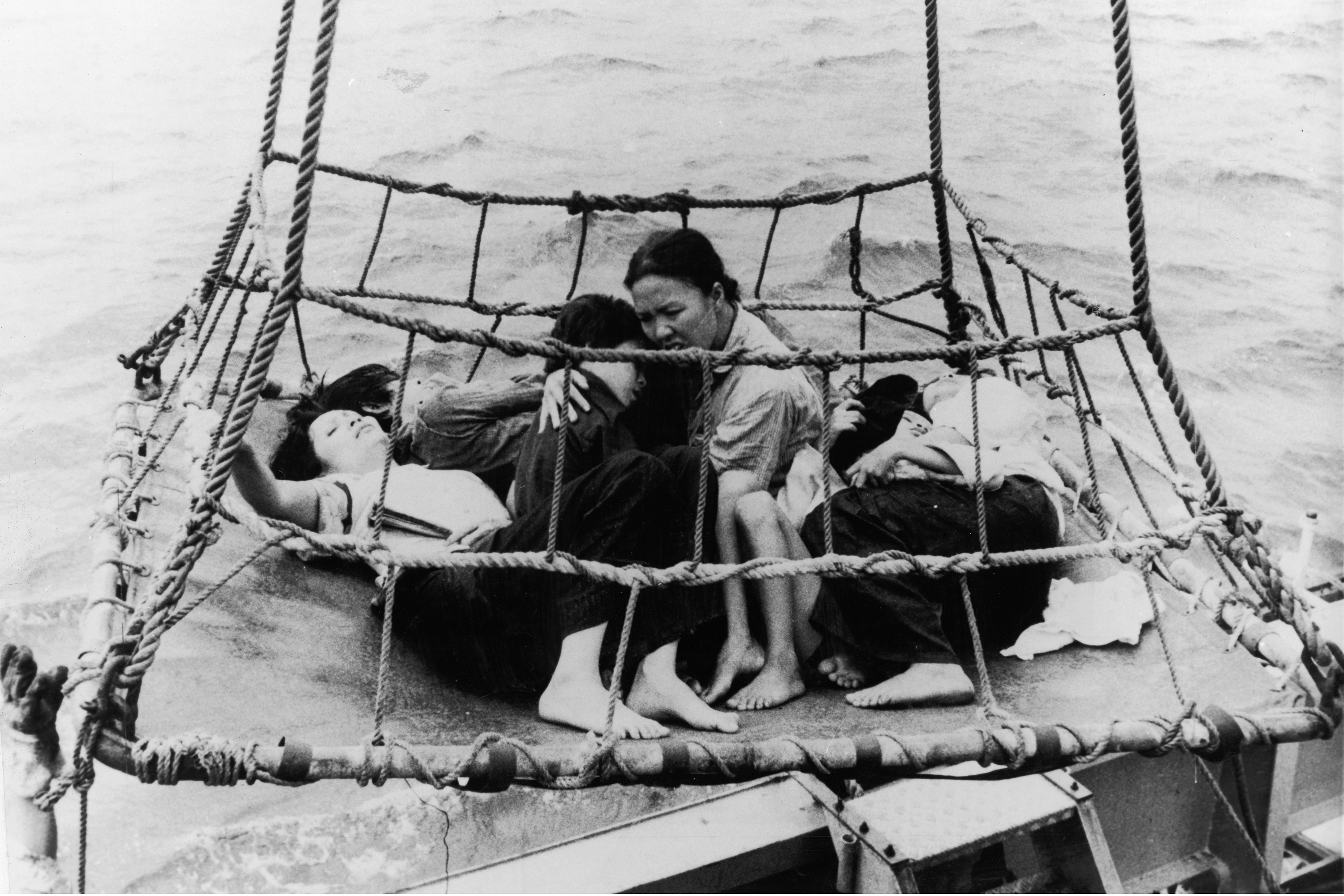 Vietnamese 'boat people' refugees huddle together on a tarp as they are airlifted out of the sea during the Vietnam War, 1960s. (Photo by Express Newspapers/Getty Images)