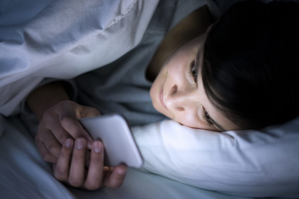 Woman using her phone under blanket in bed at night. (Getty Images)