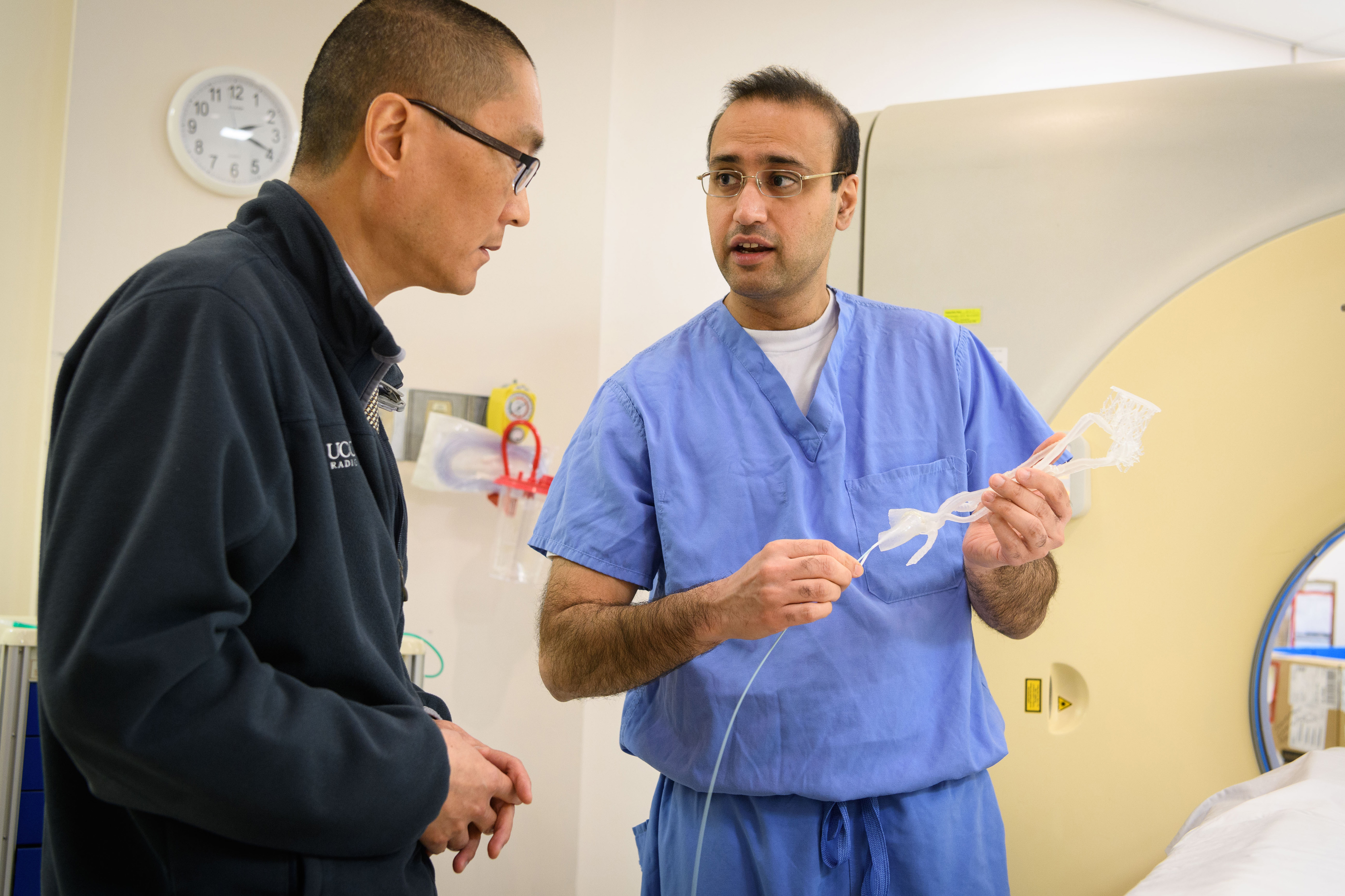 Dr. Charan K. Singh, right, holds a 3-D printed model of arteries and a catheter while speaking with Dr. Clifford Yang at UConn Health. (Peter Morenus/UConn Photo)