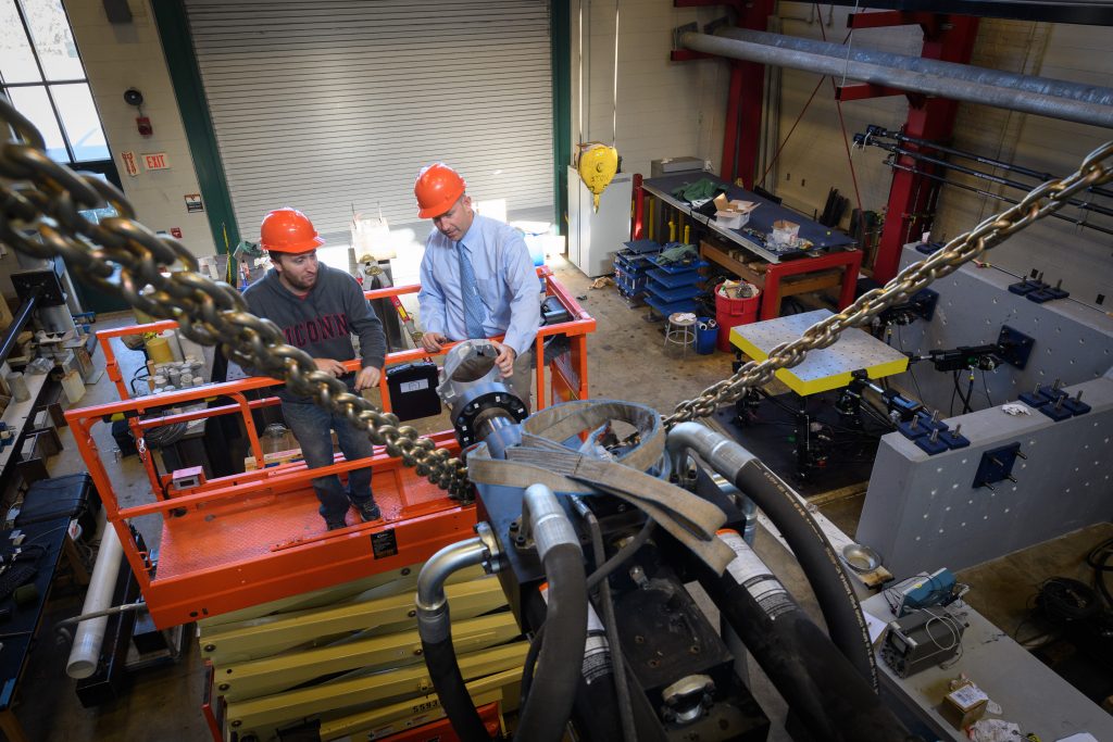 Richard Christenson,professor of civil and environmental engineering, right, and Michael Harris '10 (ENG) '13 MENG, a Ph.D. student, attach a mounting ring to a hydraulic ram in the lab at the Castelman Building on Oct. 19, 2017. (Peter Morenus/UConn Photo)