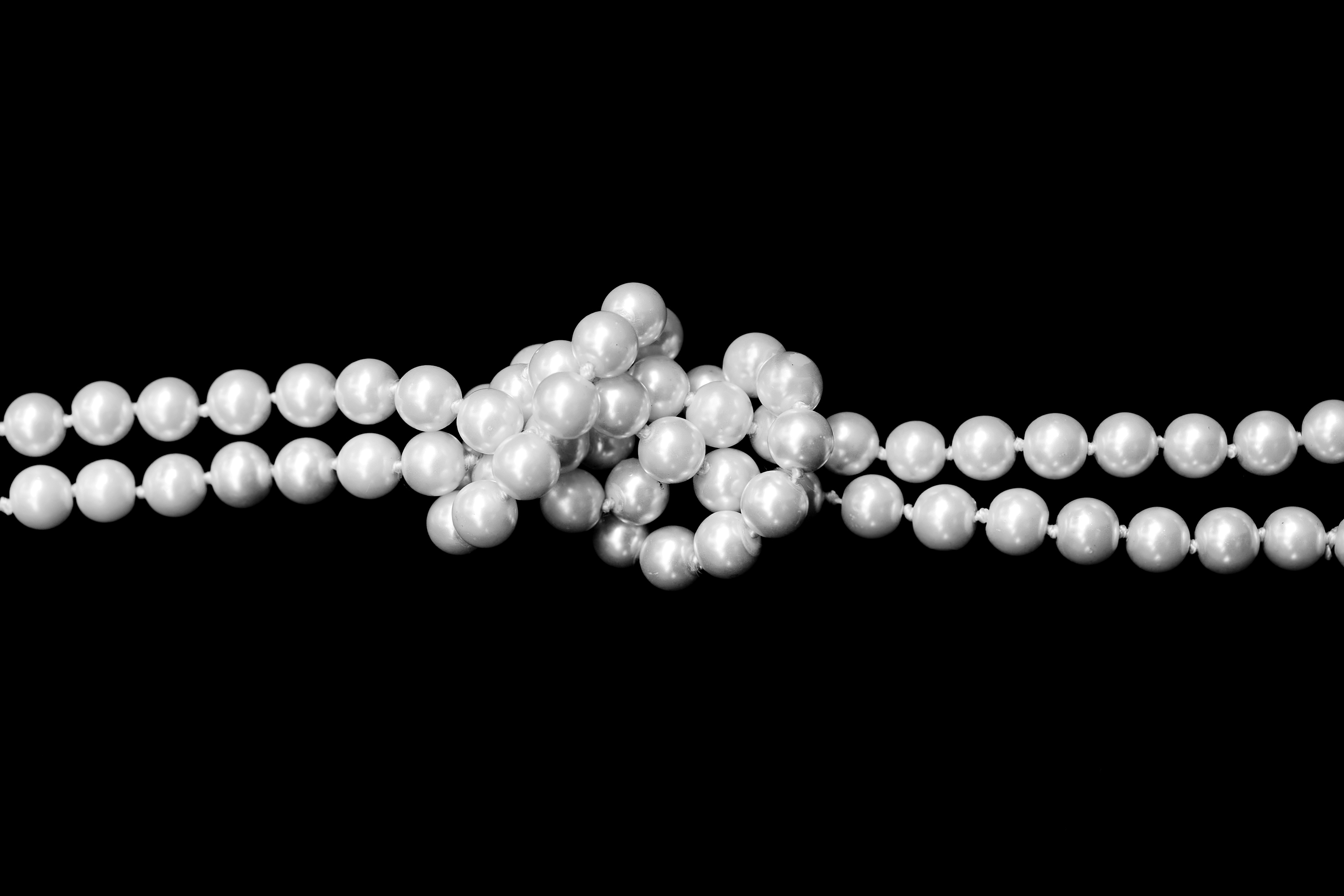 Double strand of pearls tied in a knot over black background. Chromosomes look like long necklaces of DNA in the center of every cell in the body. Some parts of the necklace are open and loose, others are coiled tightly. New research shows that as we age, some sections of our chromosomes curl and close up, making it harder for cells to access genes critical to defense against disease. (Getty Images)