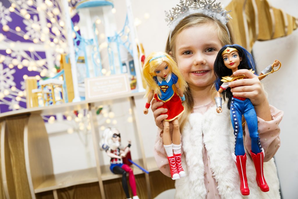 A little girl holds up Supergirl, left, and Wonder Woman, two characters from Mattel's DC Super Hero Girls collection. The appearance and dress of the new generation of fashion doll characters is a departure from Barbie’s idealized image and has changed the way children play, according to graduate student Sara Austin. (Tristan Fewings/Getty Images)