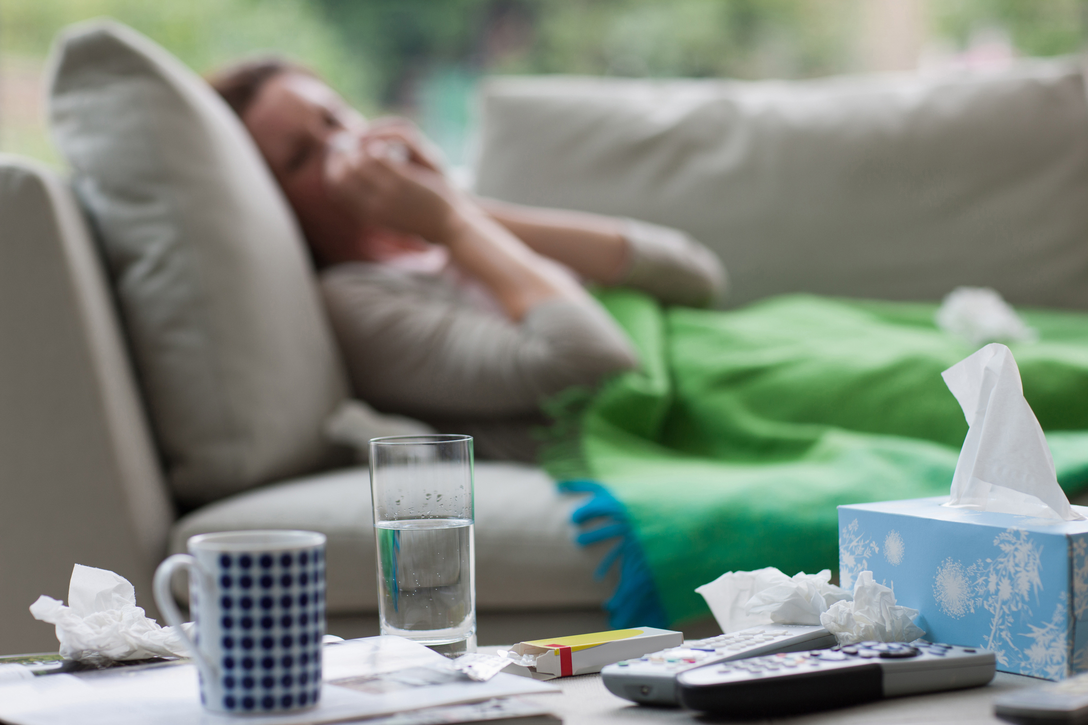 Sick woman laying on sofa blowing nose. (Getty Images)