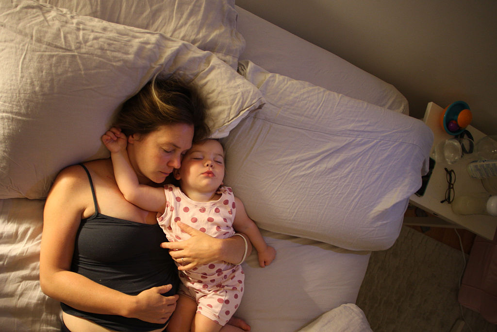 An 18-month-old girl is cuddled by her mother while asleep in bed. (Photo by Tim Clayton/Corbis via Getty Images)