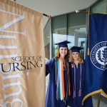 Kelly McGovern '18 (NUR), left, and Taylor Varrato '18 (NUR) hold the school banners at the Carolyn Ladd Widmer Wing of Storrs Hall before the start of the School of Nursing Commencement procession. (Peter Morenus/UConn Photo)