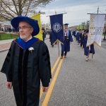Headley Freake, professor of nutritional sciences, leads the banners during the College of Agriculture, Health, and Natural Resources Commencement procession along Hillside Road. (Peter Morenus/UConn Photo)