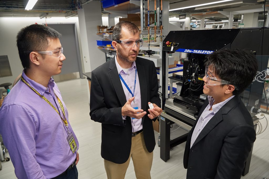 Sameh Dardona, center, principal research engineer and associate director, United Technologies Research Center, with Anson Ma, associate professor of chemical and biomolecular engineering, right, and Alan Shen, a Ph.D. student, look at a prototype wear sensor at the UTC Research Center in East Hartford on June 18, 2018. (Peter Morenus/UConn Photo)