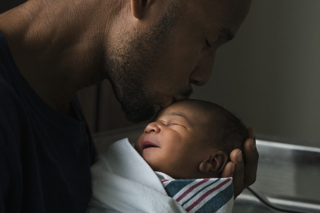 A black father kisses the forehead of his newborn son. (Ariel Skelley/Getty Images)