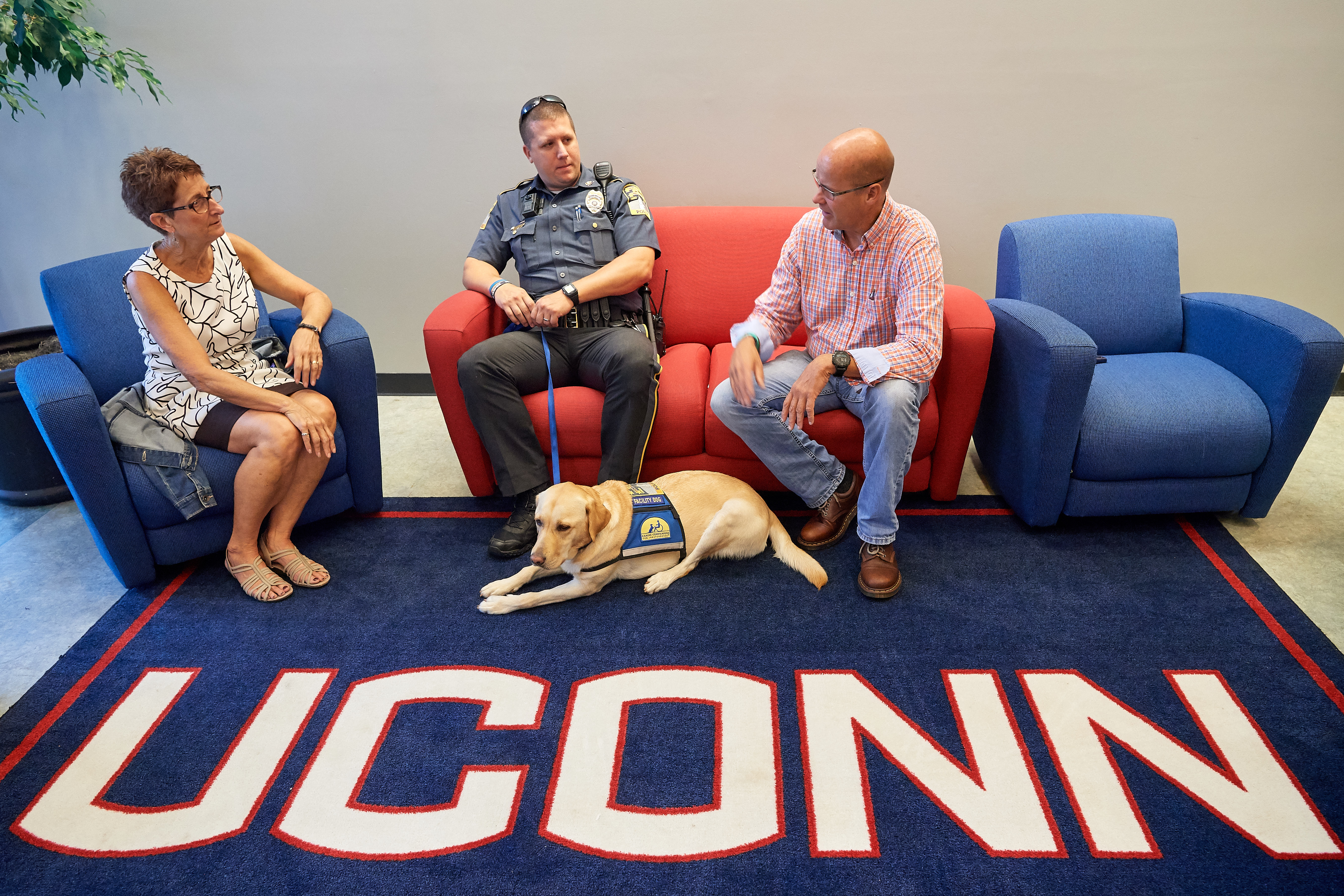 Sharon Mendes, left, with Officer Justin Cheney '07 (CLAS) and the police department's community outreach dog Tildy, and Paul Hanlon '15 (BGS), '17 MS, '19 MBA at the Student Union on Sept. 18, 2018. (Peter Morenus/UConn Photo)