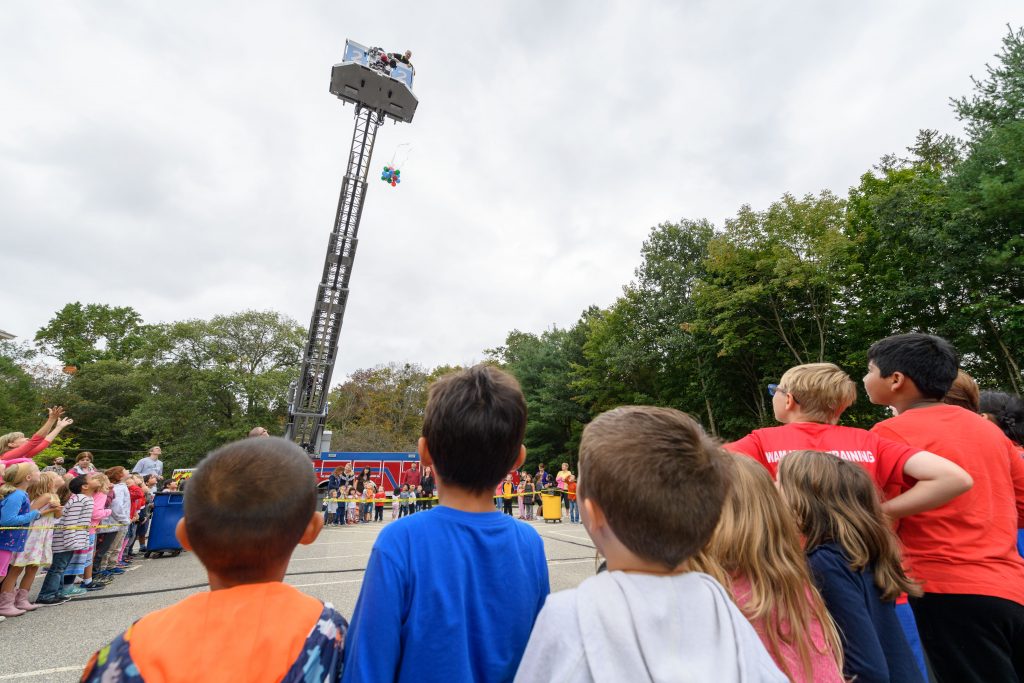 Students, teachers, and parents look on as UConn firefighters atop their ladder truck drop eggs with creative forms of protection developed by students at Goodwin Elementary School in Mansfield on Sept. 21, 2018. (Peter Morenus/UConn Photo)