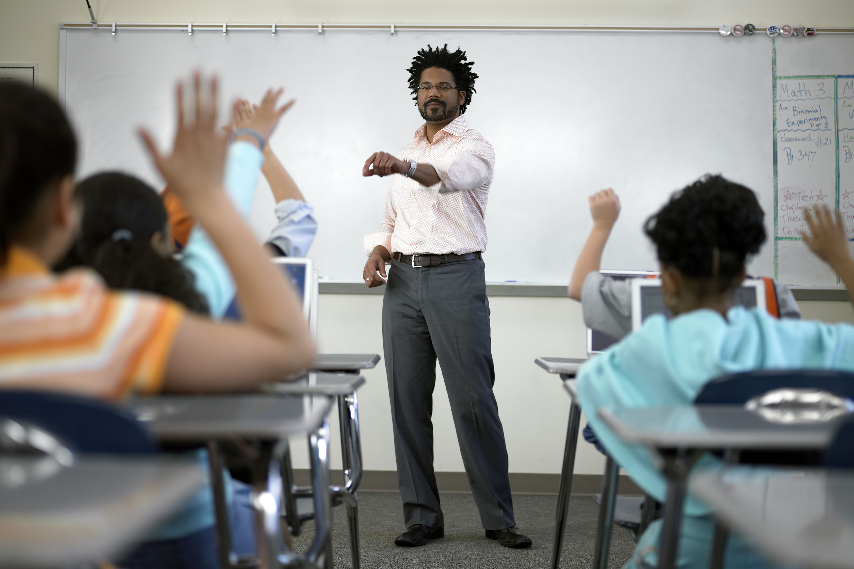 African-American male teacher standing before students (8-10) with hands raised. (Getty Images)