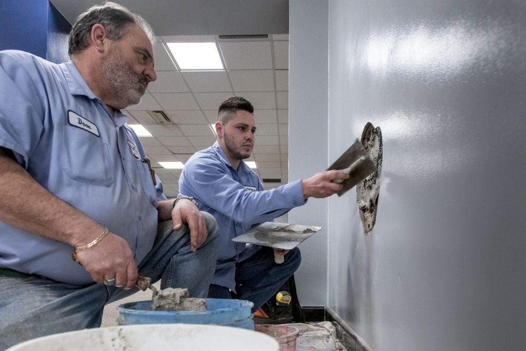 Longtime UConn mason Dave Prouty, left, looks on as 'new guy' Connor Adams, a UConn employee since 2017, repairs a wall in Shippee Hall. (Sean Flynn/UConn Photo)
