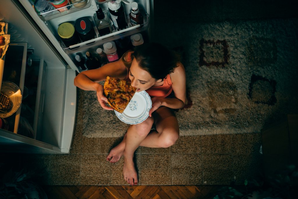 A young woman eating pizza in front of the refrigerator late at night. (Getty Images)