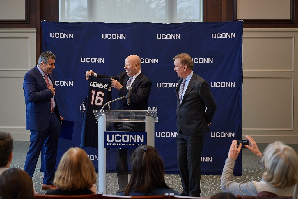 Thomas Katsouleas, left, reacts as he is presented with a basketball jersey by board chair Thomas Kruger, center, and Gov. Ned Lamont at a press conference following his appointment to be the 16th president of the University of Connecticut. (Peter Morenus/UConn Photo)