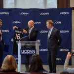 Thomas Katsouleas, left, reacts as he is presented with a basketball jersey by board chair Thomas Kruger, center, and Gov. Ned Lamont at a press conference following his appointment to be the 16th president of the University of Connecticut on Feb. 5, 2019. (Peter Morenus/UConn Photo)