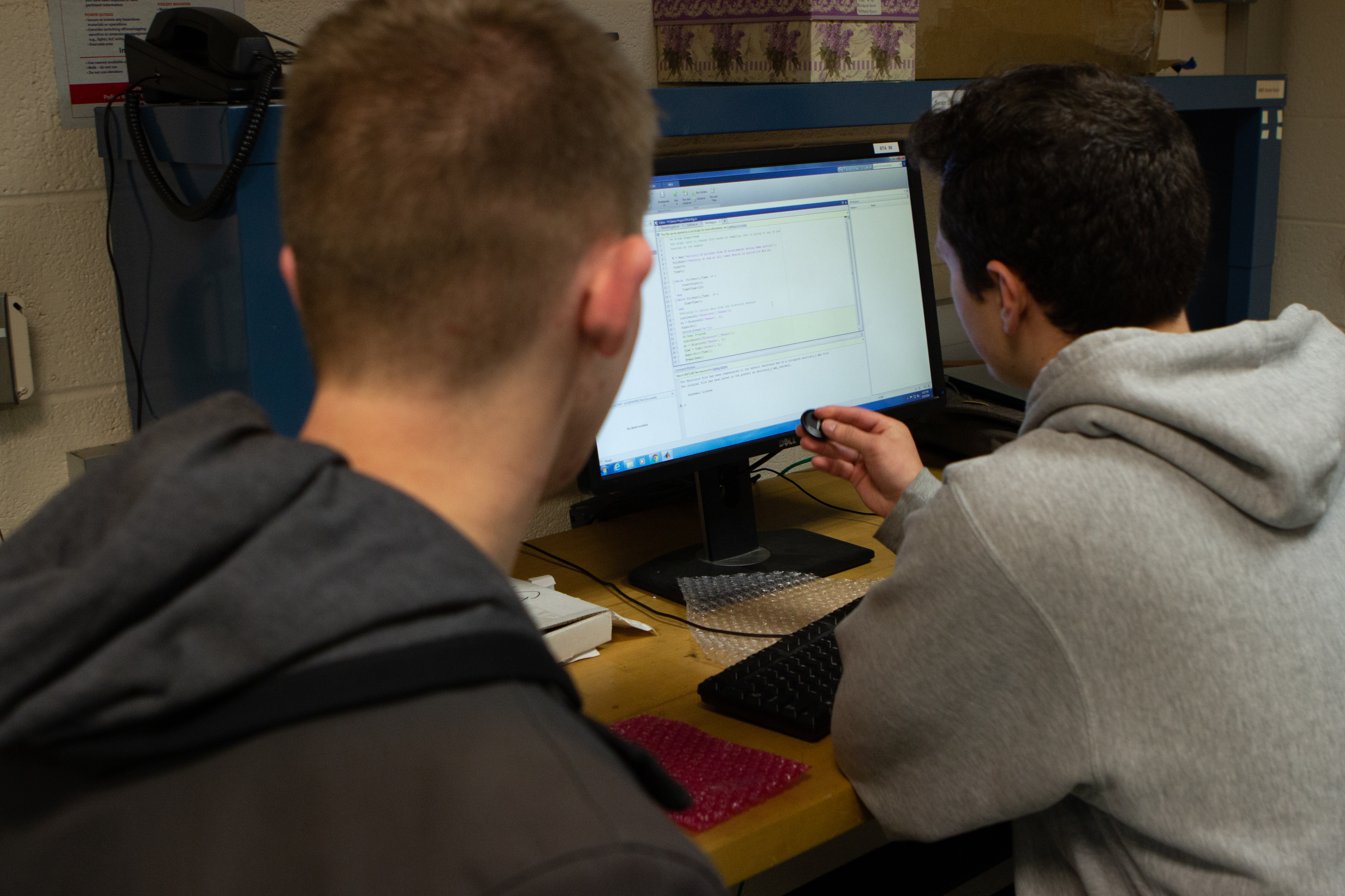 Gutowski (left) and Hill (right) study their coding work, while Hill holds the crucial bluetooth sensor used in the device. (Eli Freund/UConn Photo)
