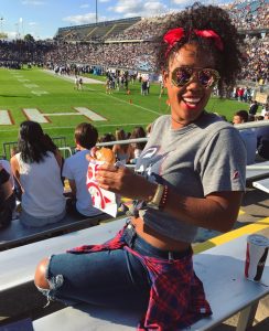 Danielle Fontaine enjoying a UConn Football game from the stands, while holding a sandwich.
