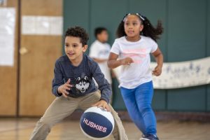 Third-grader Ediel Lopez-Torres, with the ball, and first-grader Stella Flores play basketball in a game against the teachers at Kennelly School on May 2, 2019. (Sean Flynn/UConn Photo)